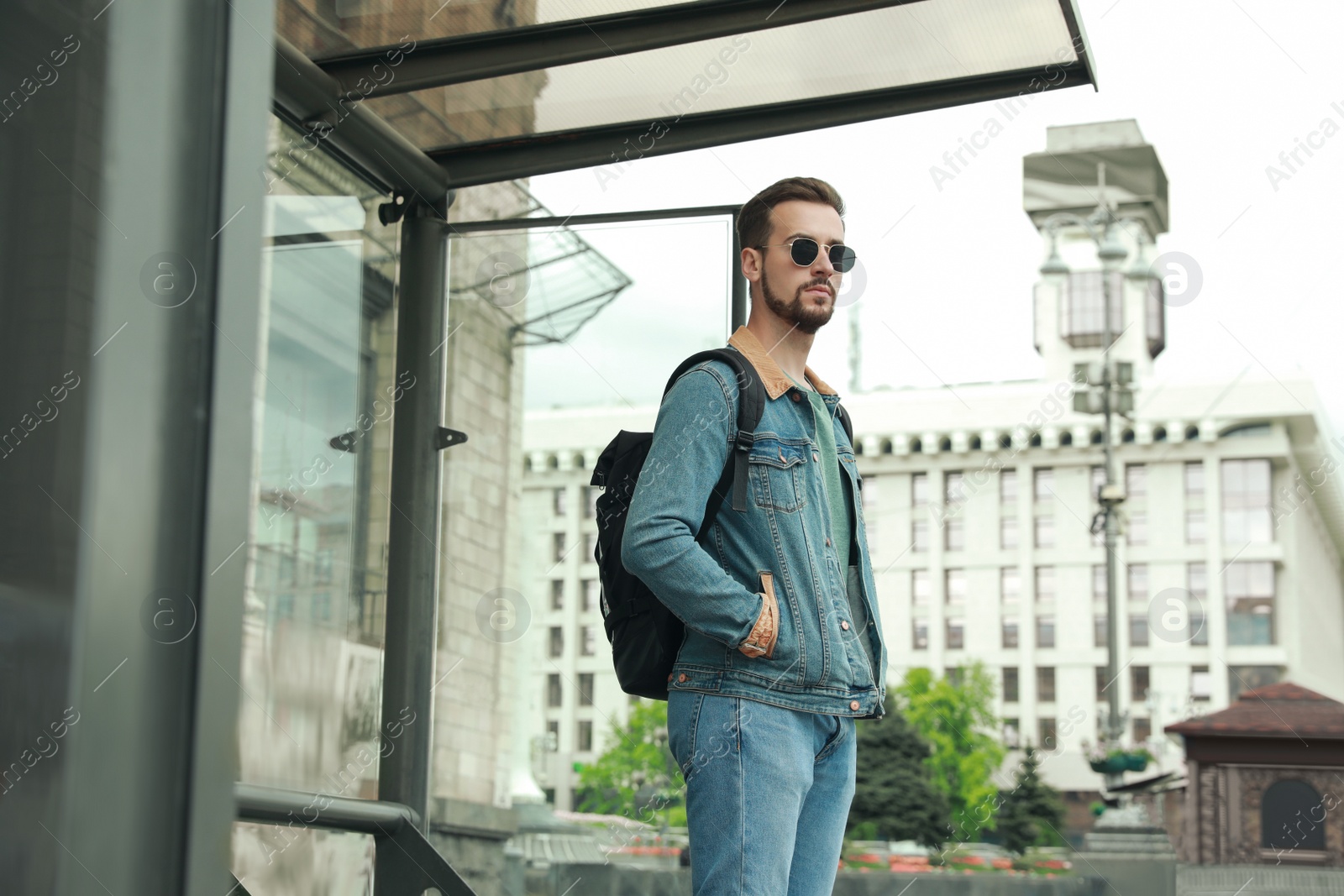 Photo of Young man with backpack waiting for public transport at bus stop