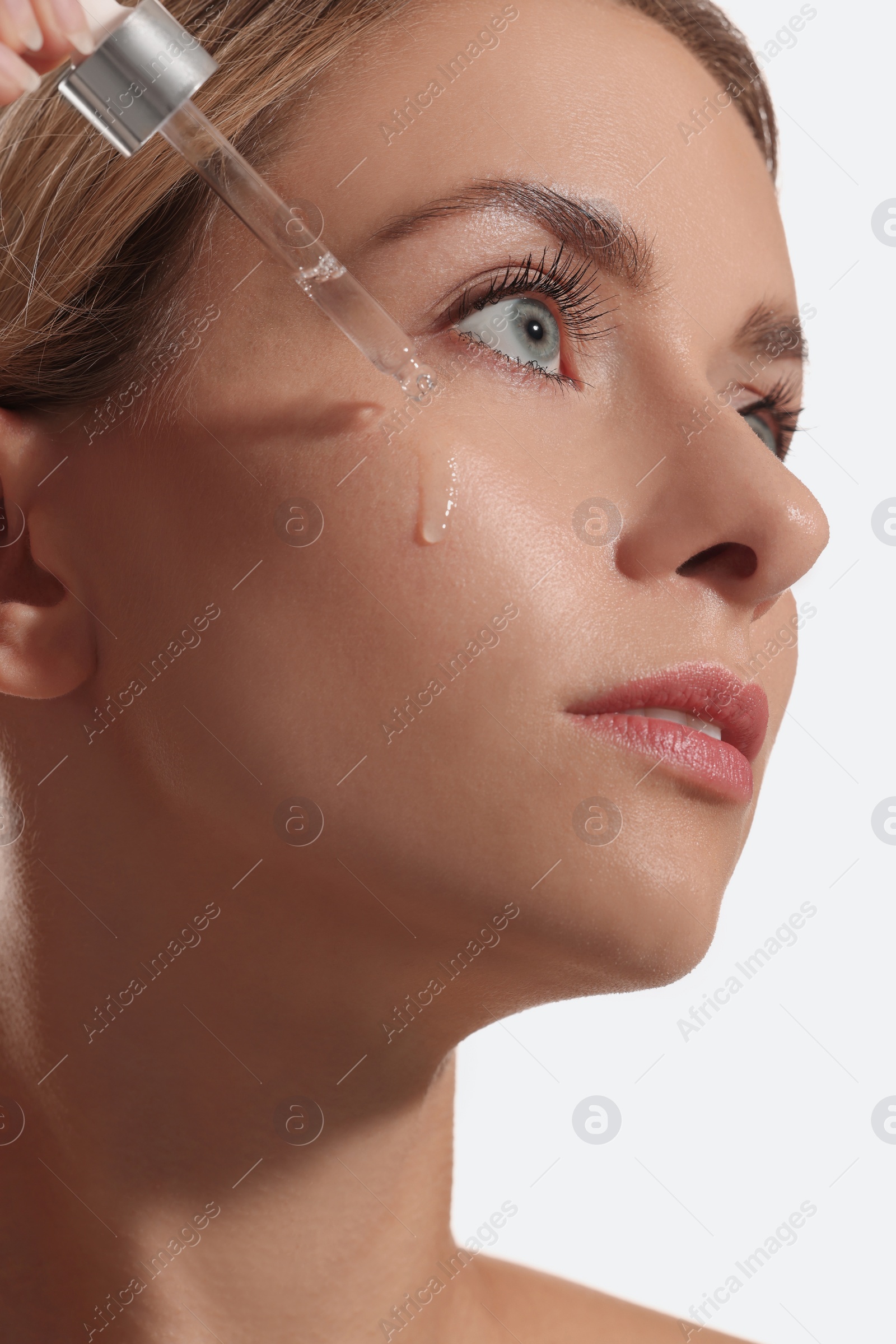 Photo of Beautiful woman applying cosmetic serum onto her face on white background, closeup