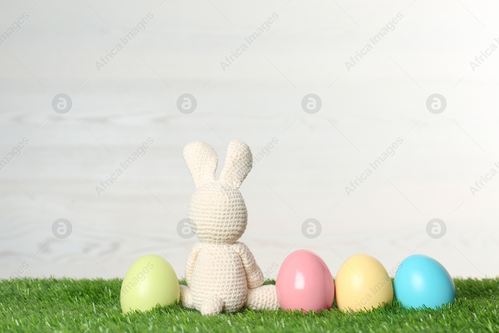 Photo of Cute Easter bunny toy and dyed eggs on green grass, space for text