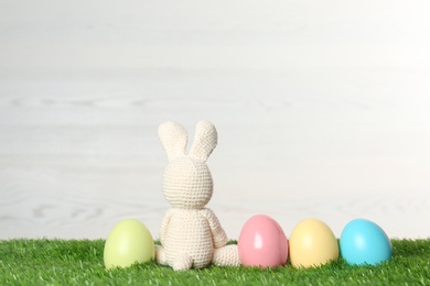 Photo of Cute Easter bunny toy and dyed eggs on green grass, space for text