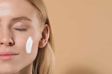 Beautiful young woman with sun protection cream on her face against beige background, closeup. Space for text