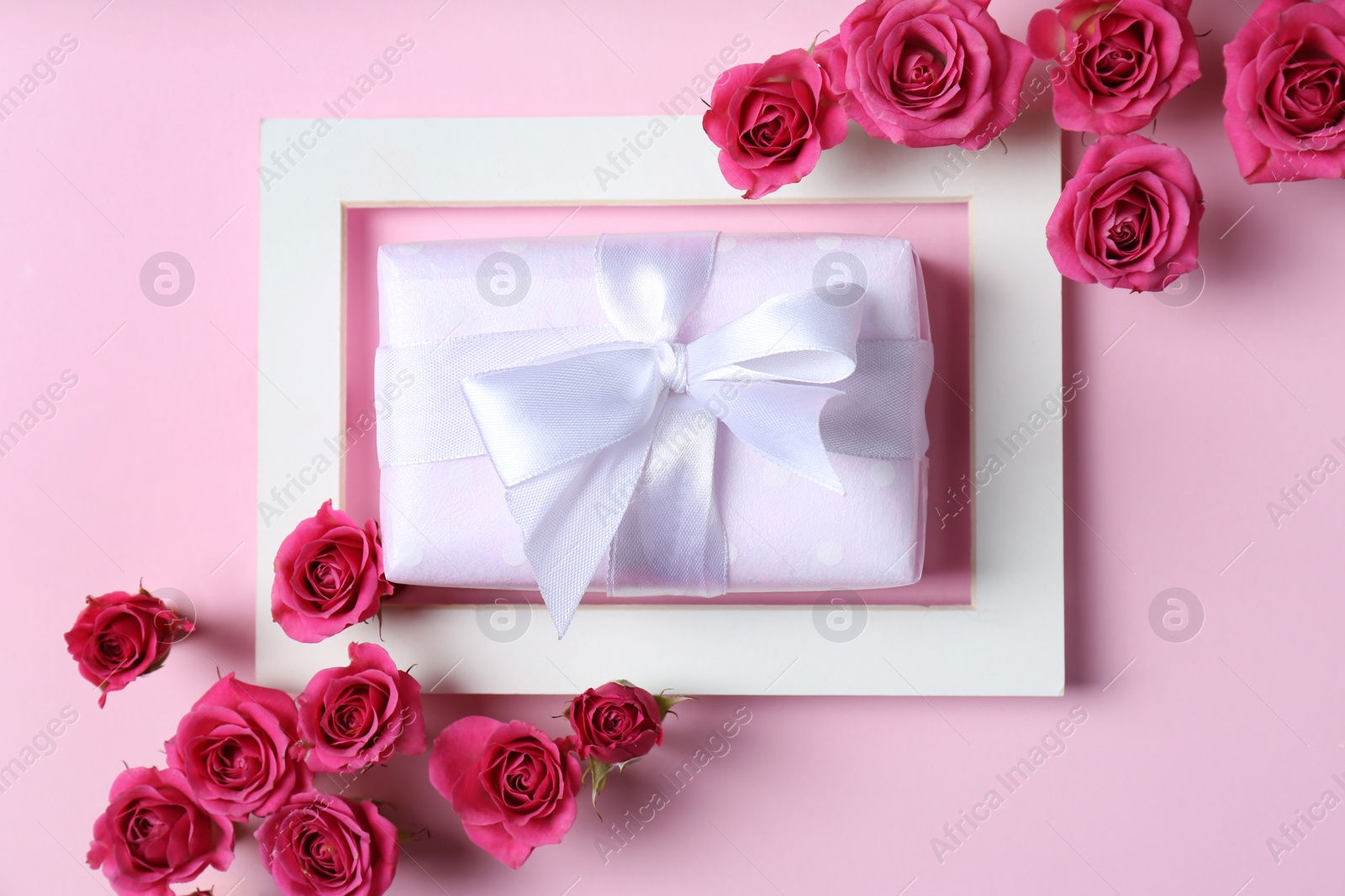 Photo of Frame with roses and gift box on color background, top view