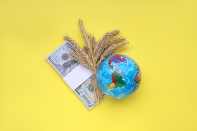 Photo of Import and export concept. Globe, ears of wheat and money on yellow background, flat lay