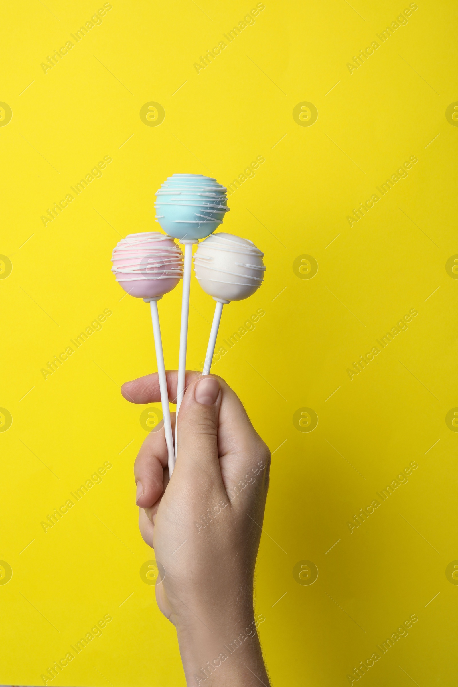 Photo of Woman holding sweet cake pops on yellow background, closeup