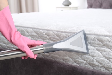 Woman disinfecting mattress with vacuum cleaner, closeup. Space for text