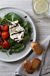 Photo of Delicious burrata cheese served with tomatoes, croutons, arugula and basil on white wooden table, flat lay