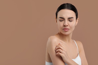 Woman with dry skin checking her arm on beige background, space for text