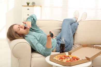 Photo of Lazy young woman with pizza and drink watching TV at home