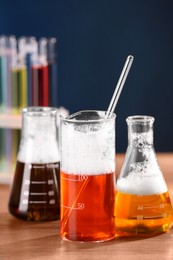 Photo of Laboratory glassware with colorful liquids on wooden table, closeup. Chemical reaction