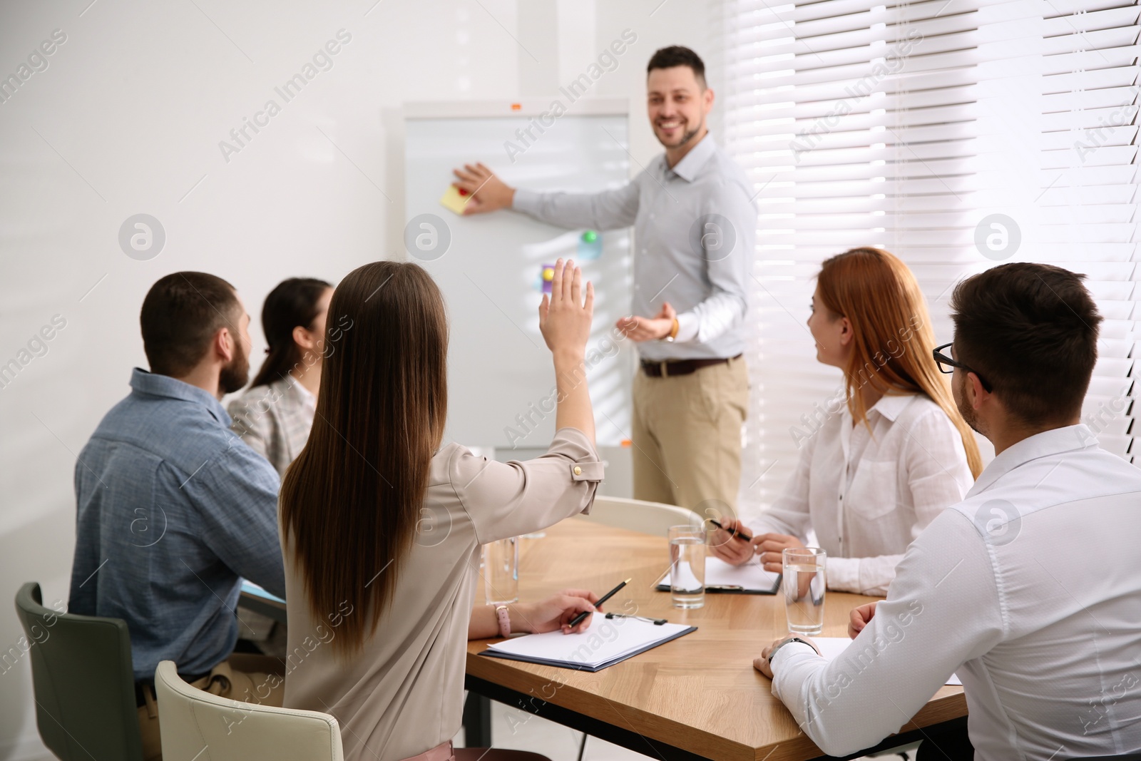 Photo of Young woman raising hand to ask question at business training in conference room