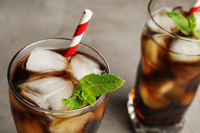 Photo of Glasses of refreshing soda drink with ice cubes and straws on grey background, closeup. Space for text