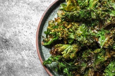 Photo of Tasty baked kale chips on grey table, closeup