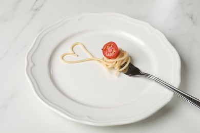 Photo of Heart made of tasty spaghetti, fork and tomato on white marble table