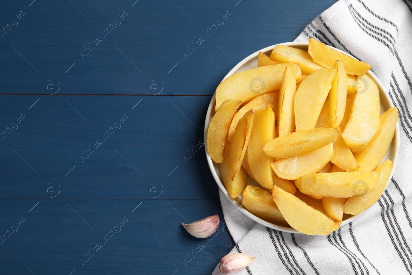 Photo of Plate with tasty baked potato wedges on blue wooden table, flat lay. Space for text
