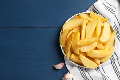 Plate with tasty baked potato wedges on blue wooden table, flat lay. Space for text