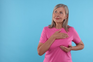 Photo of Beautiful senior woman doing breast self-examination on light blue background, space for text
