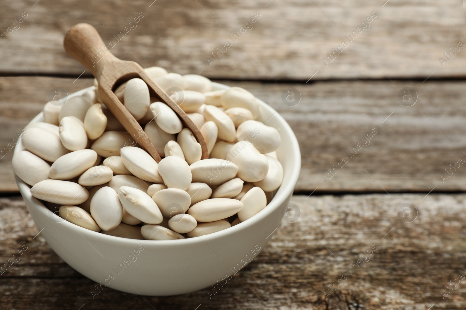 Photo of Bowl and scoop with uncooked white beans on wooden table, space for text