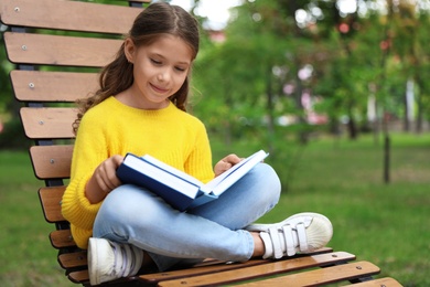 Cute little girl reading book on lounger in park