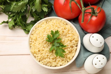 Photo of Delicious bulgur with parsley in bowl, tomatoes and spices on wooden table, top view. Space for text