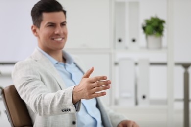 Businessman offering handshake in office, focus on hand. Space for text