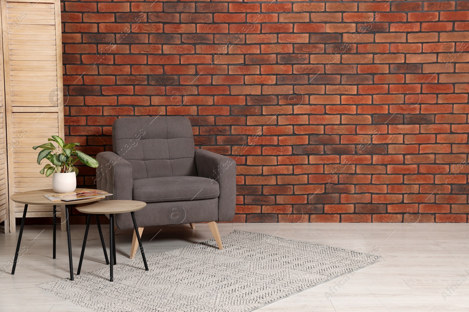 Photo of Cosy armchair and potted plant on coffee table near brick wall in room, space for text. Interior design