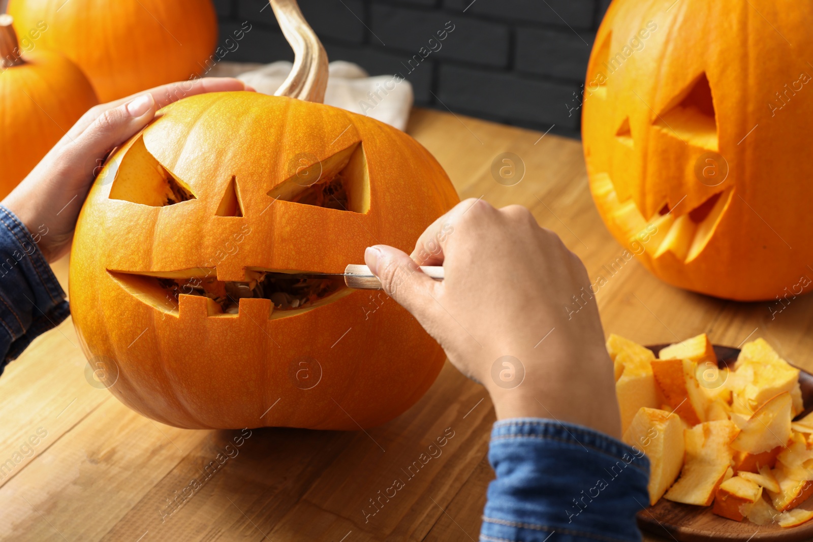 Photo of Woman carving pumpkin at wooden table, closeup. Halloween celebration