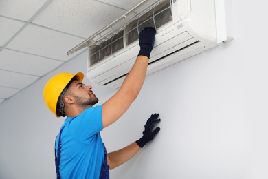 Professional technician maintaining modern air conditioner indoors