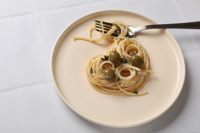 Photo of Heart made of tasty spaghetti, fork, olives and cheese on white tiled table