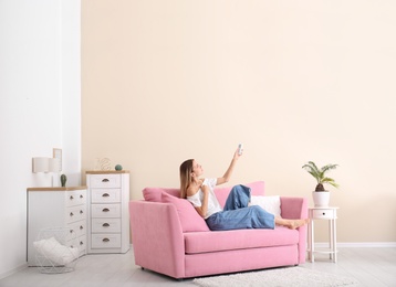 Young woman operating air conditioner with remote control at home