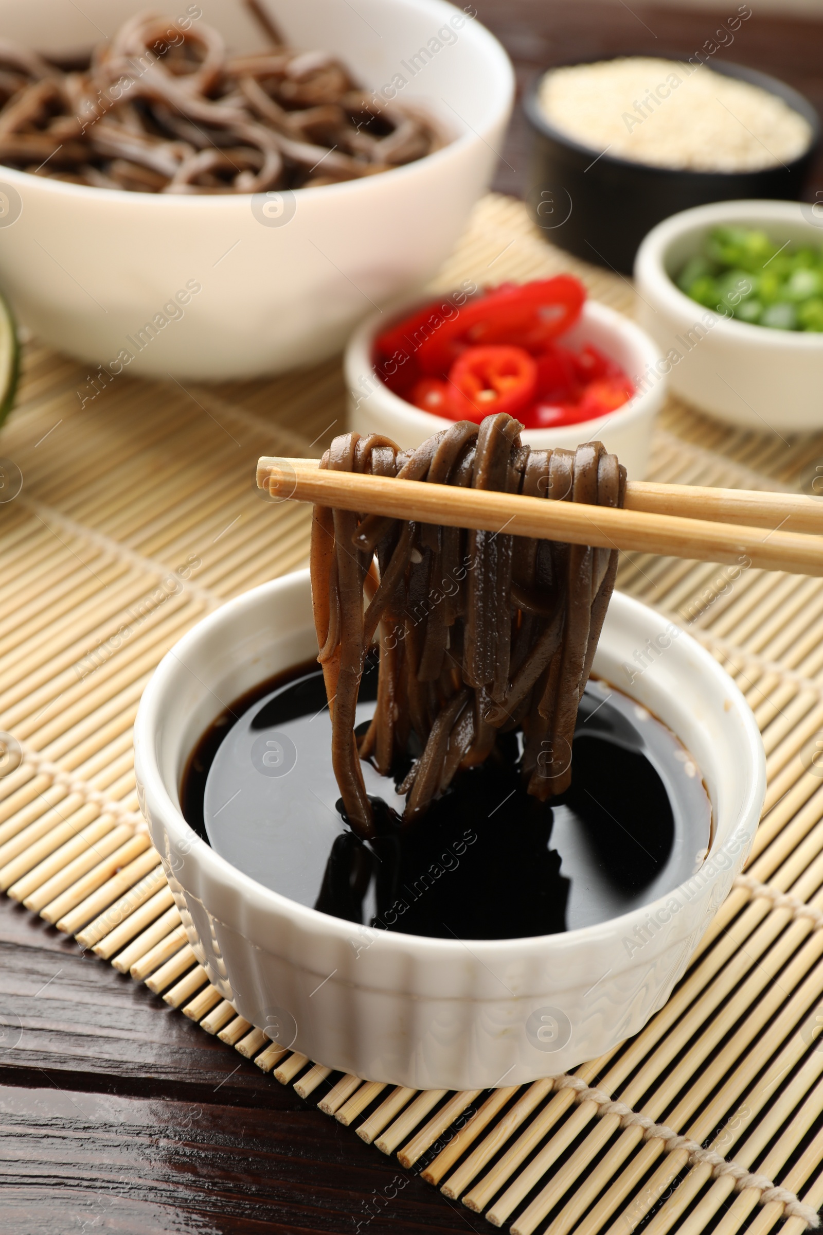 Photo of Eating delicious buckwheat noodles (soba) with chopsticks at wooden table, closeup