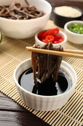 Photo of Eating delicious buckwheat noodles (soba) with chopsticks at wooden table, closeup