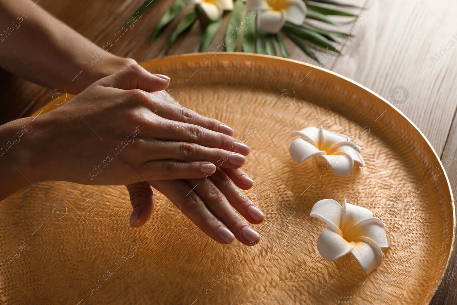 Photo of Woman soaking her hands in bowl of water and flowers on table, closeup with space for text. Spa treatment