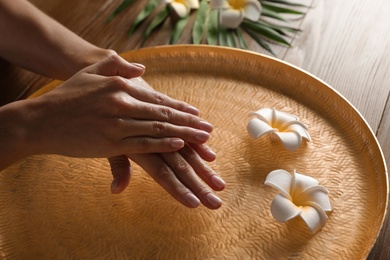 Photo of Woman soaking her hands in bowl of water and flowers on table, closeup with space for text. Spa treatment