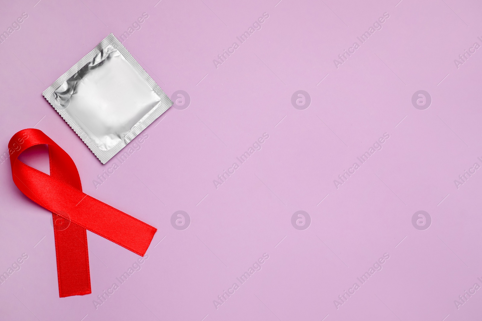 Photo of Red ribbon and condom on violet background, flat lay with space for text. AIDS disease awareness