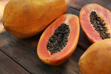 Photo of Fresh ripe cut and whole papaya fruits on wooden table, closeup