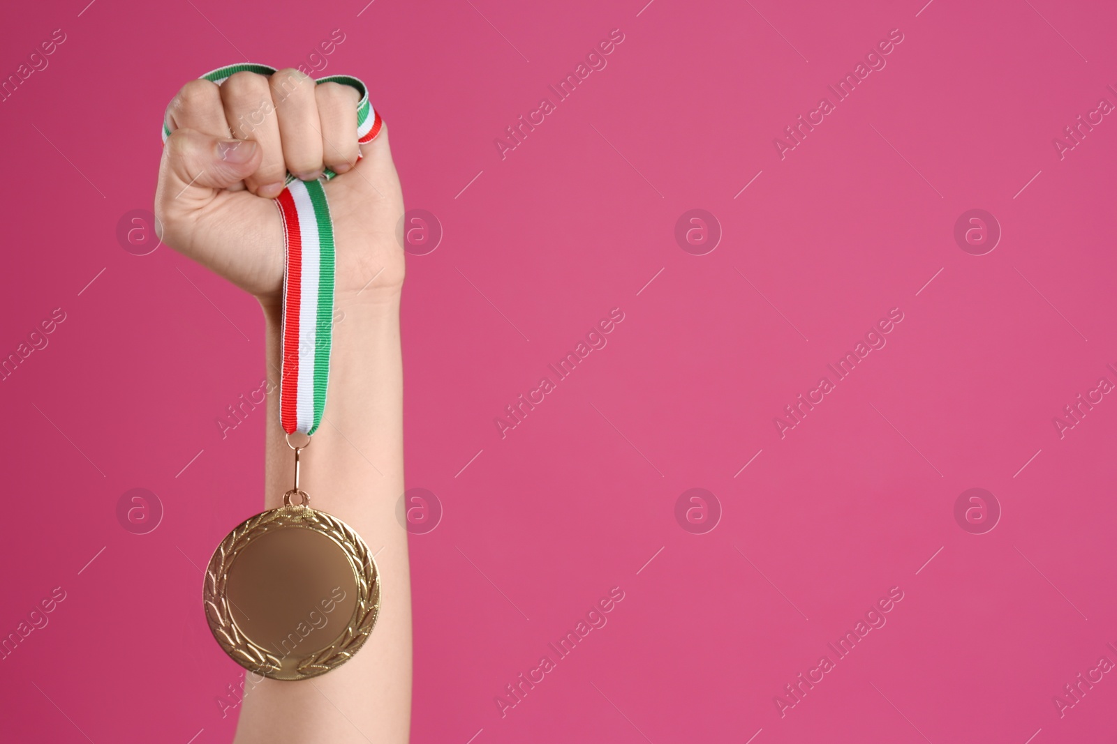 Photo of Woman holding golden medal on pink background, closeup. Space for design