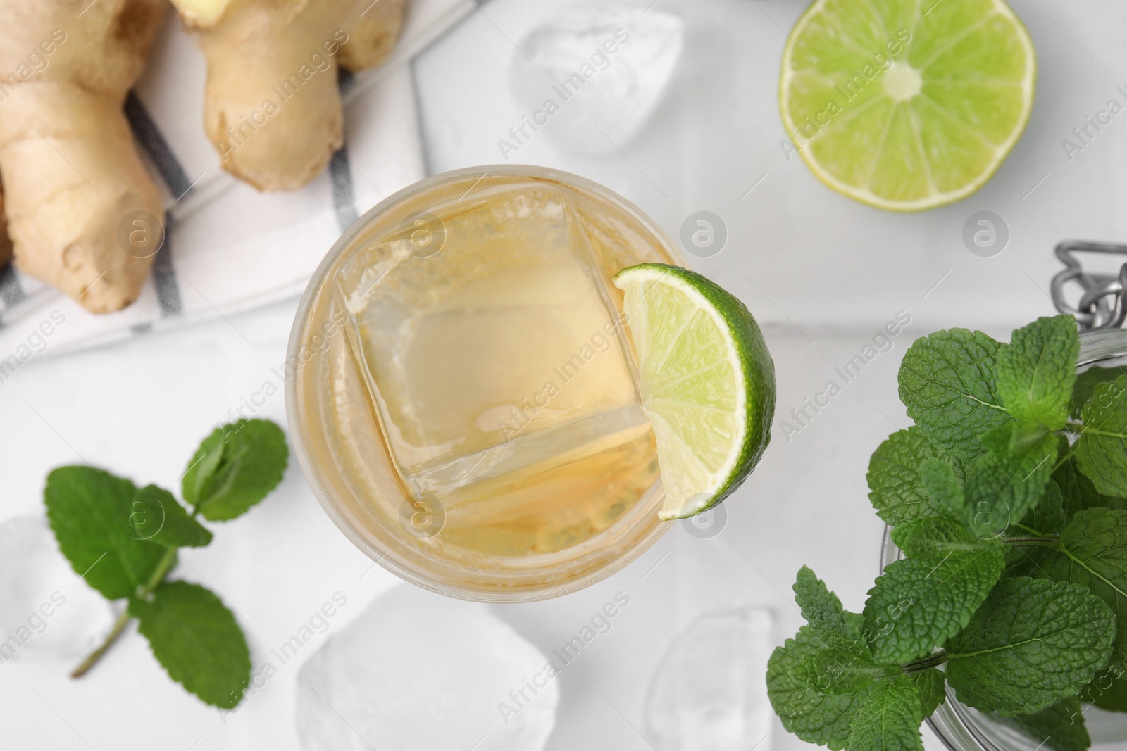 Photo of Glass of tasty ginger ale with ice cube and ingredients on white tiled table, flat lay