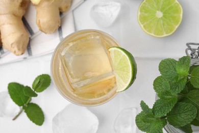 Photo of Glass of tasty ginger ale with ice cube and ingredients on white tiled table, flat lay