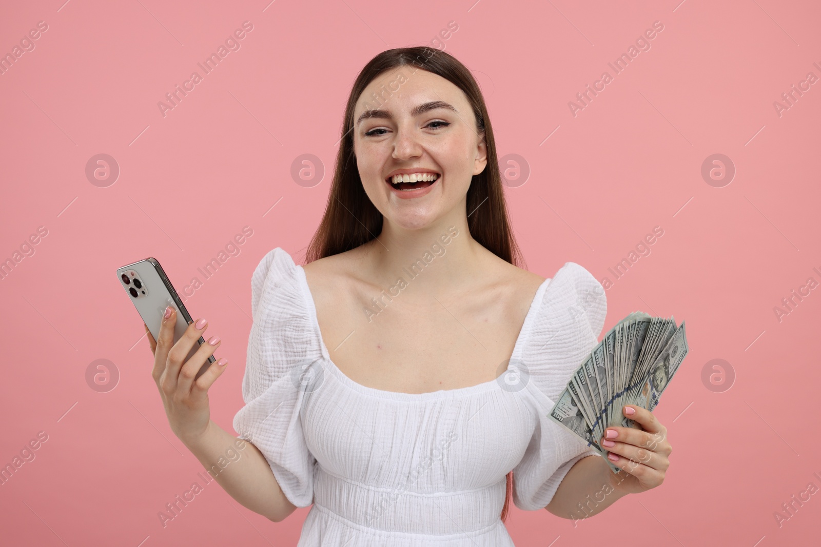 Photo of Happy woman with dollar banknotes and smartphone on pink background