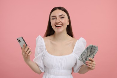 Happy woman with dollar banknotes and smartphone on pink background