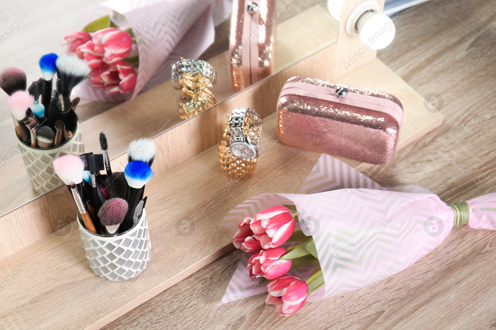 Photo of Holder with professional makeup brushes and tulip bouquet on wooden table