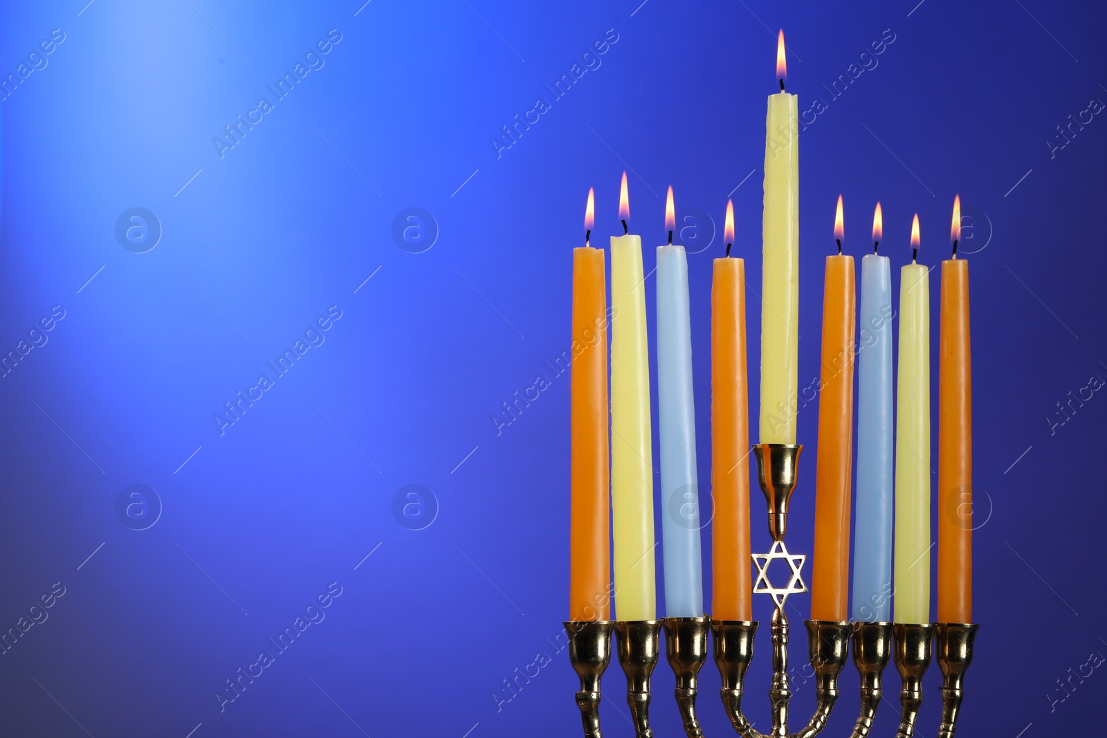 Photo of Hanukkah celebration. Menorah with burning candles on blue background, space for text