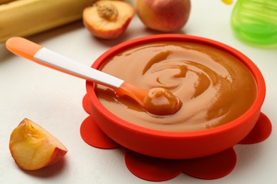Bowl and spoon with tasty pureed baby food on white table, closeup