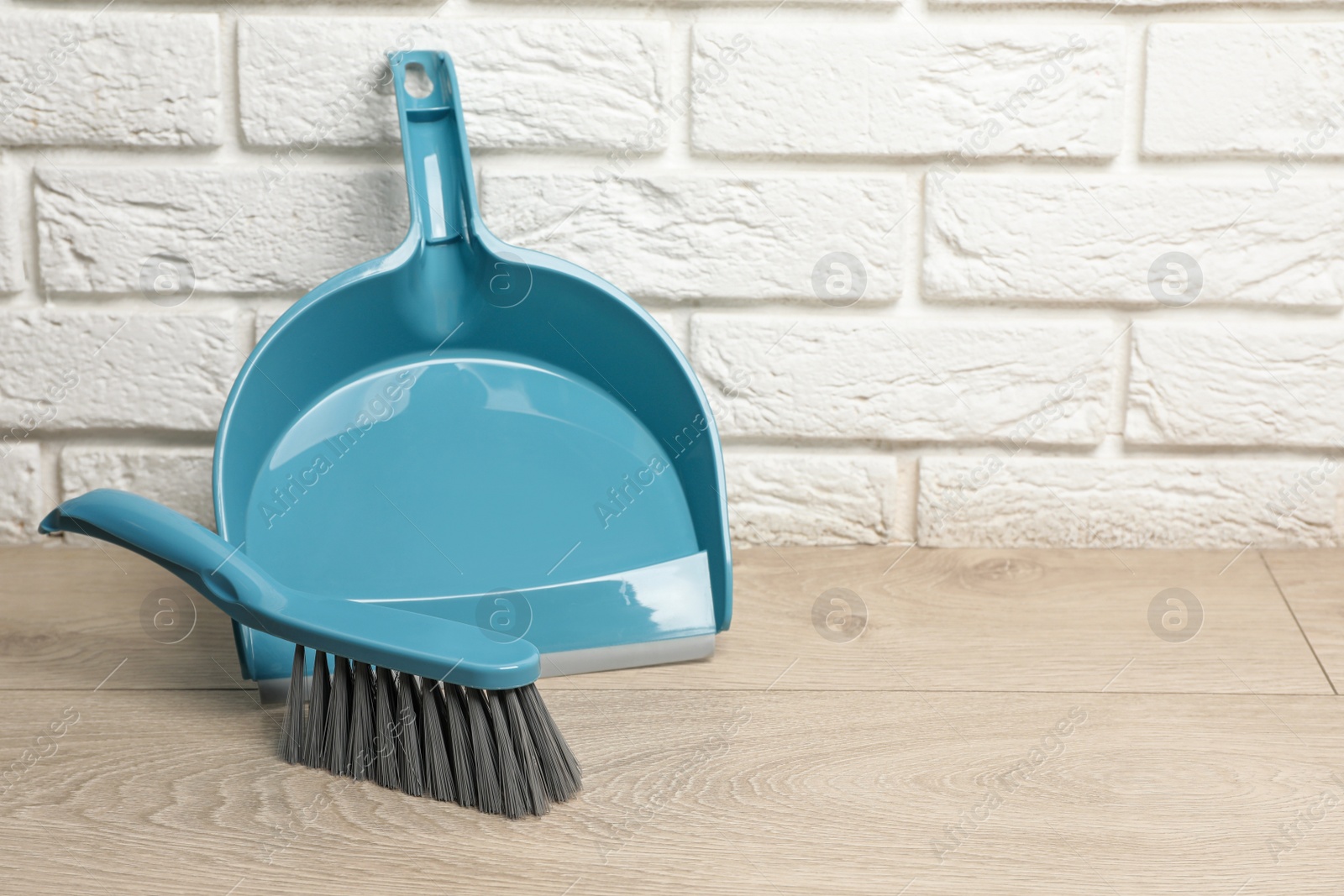 Photo of Plastic whisk broom with dustpan near white brick wall indoors. Space for text