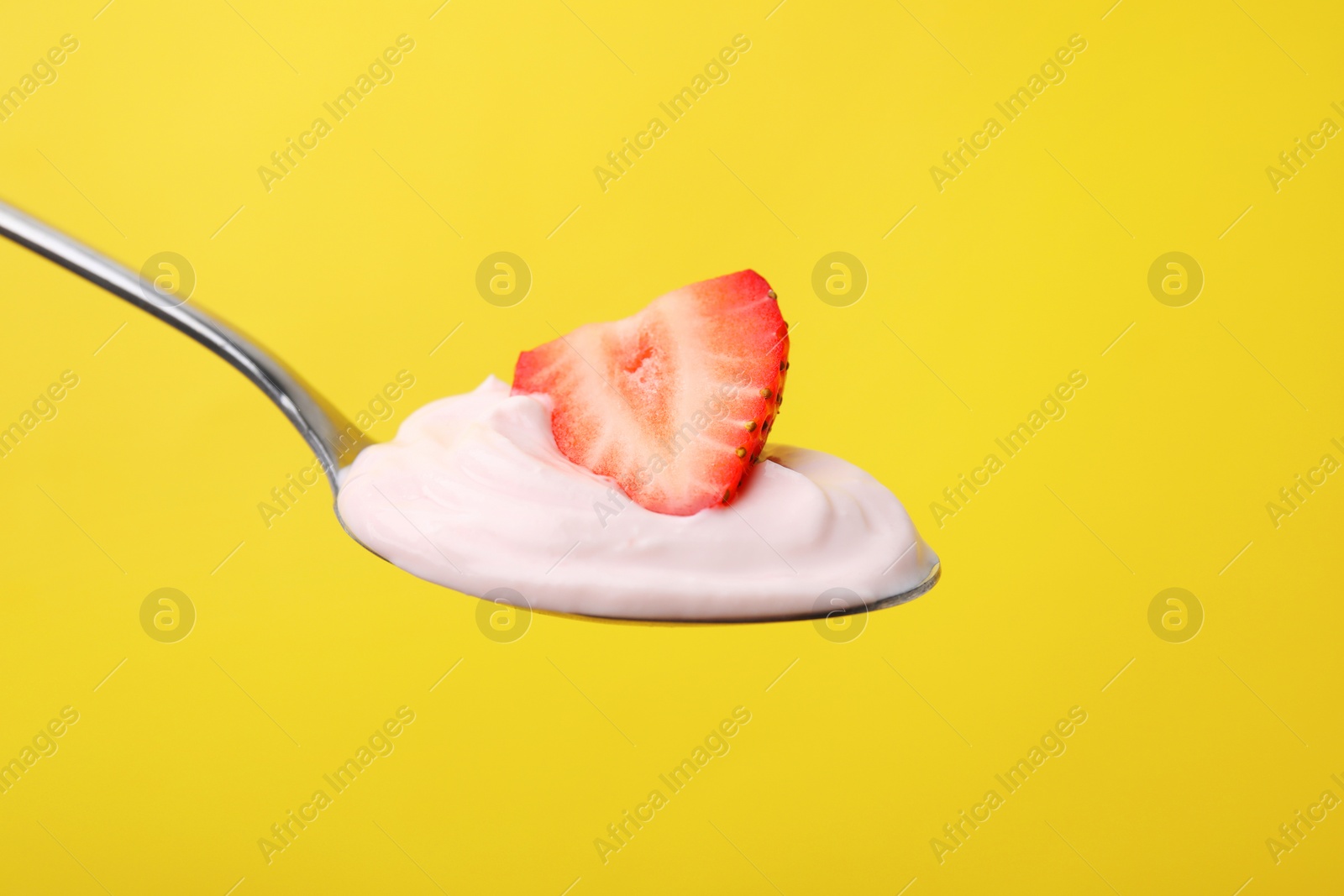 Photo of Delicious natural yogurt with fresh strawberry in spoon on yellow background