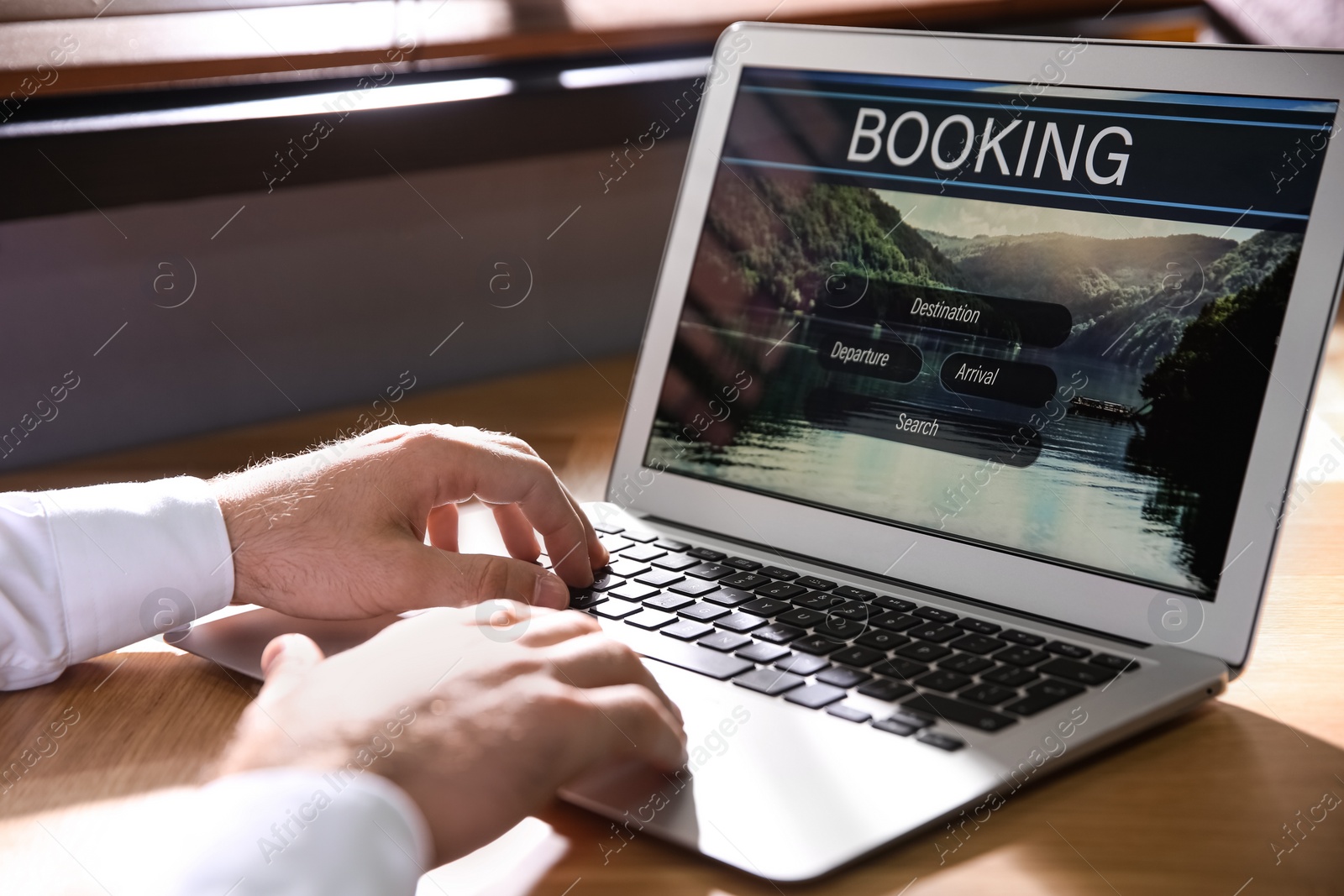 Photo of Man with laptop booking tickets online at wooden table, closeup. Travel agency concept