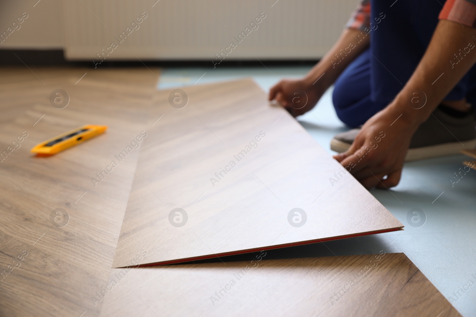 Photo of Worker installing laminated wooden floor indoors, closeup