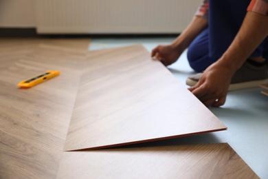 Worker installing laminated wooden floor indoors, closeup