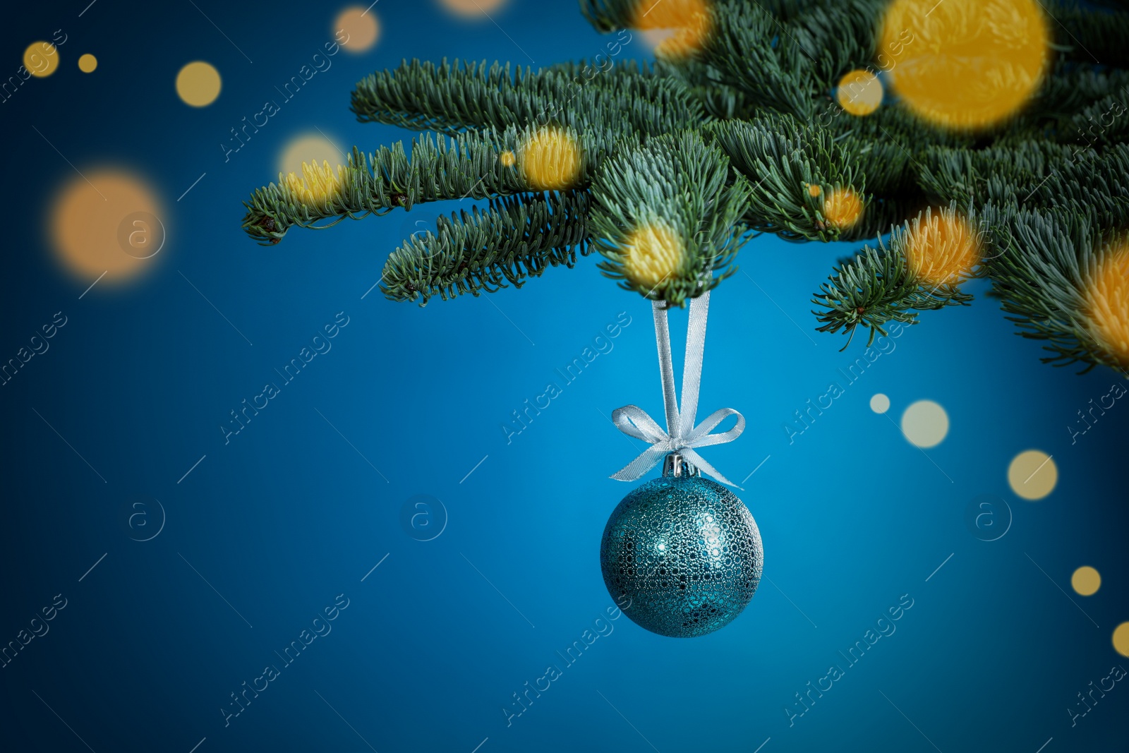 Photo of Beautiful Christmas ball hanging on fir tree branch against light blue background, bokeh effect. Space for text