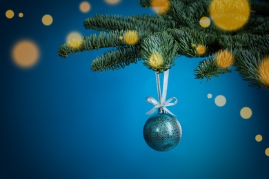 Beautiful Christmas ball hanging on fir tree branch against light blue background, bokeh effect. Space for text